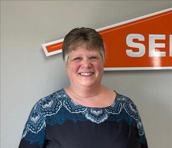 Female employee with gray hair smiling in front of a SERVPRO sign