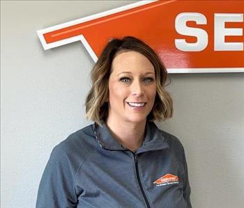 Female employee with dark hair smiling in front of a SERVPRO sign