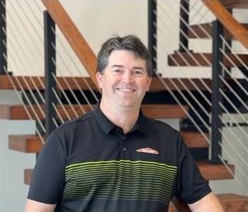 Male employee with dark hair smiling in front of SERVPRO sign