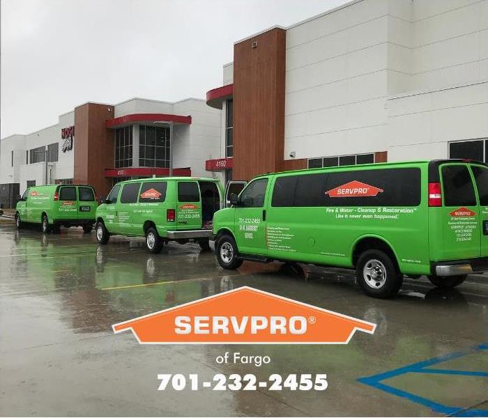 A line of bright green SERVPRO of Fargo vehicles are parked outside in the rain while responding to a storm damage emergency.